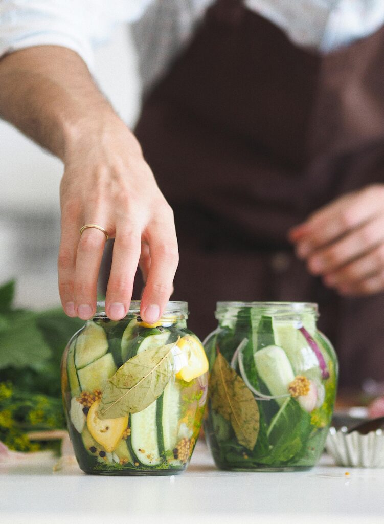 Close-up of hands preparing homemade pickled vegetables in glass jars on a kitchen counter.