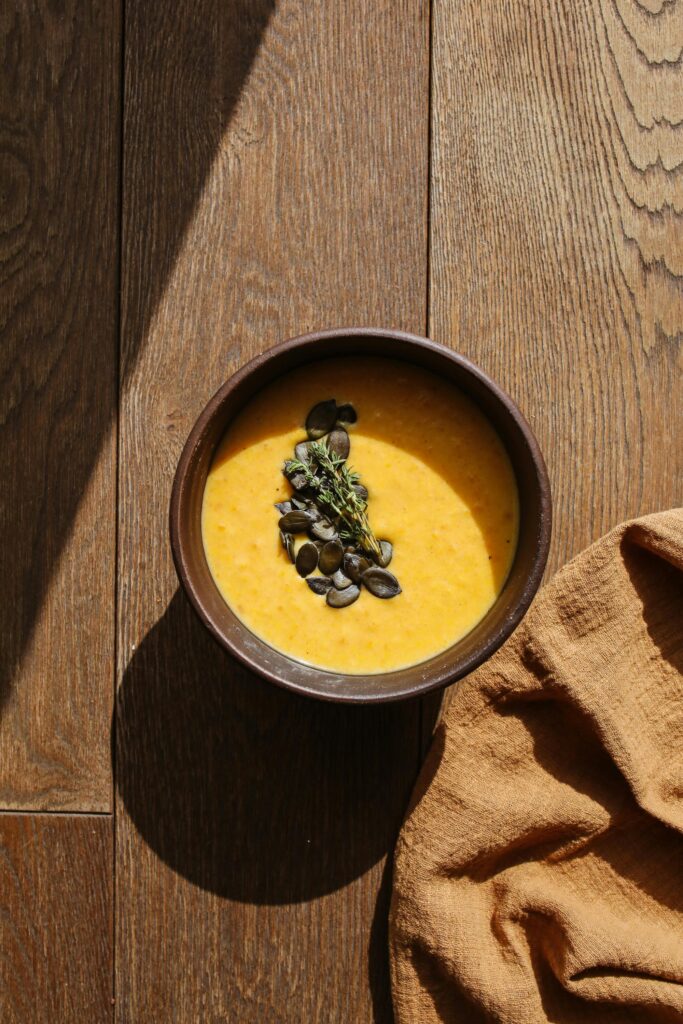 A bowl of creamy pumpkin soup garnished with seeds on a wooden table.