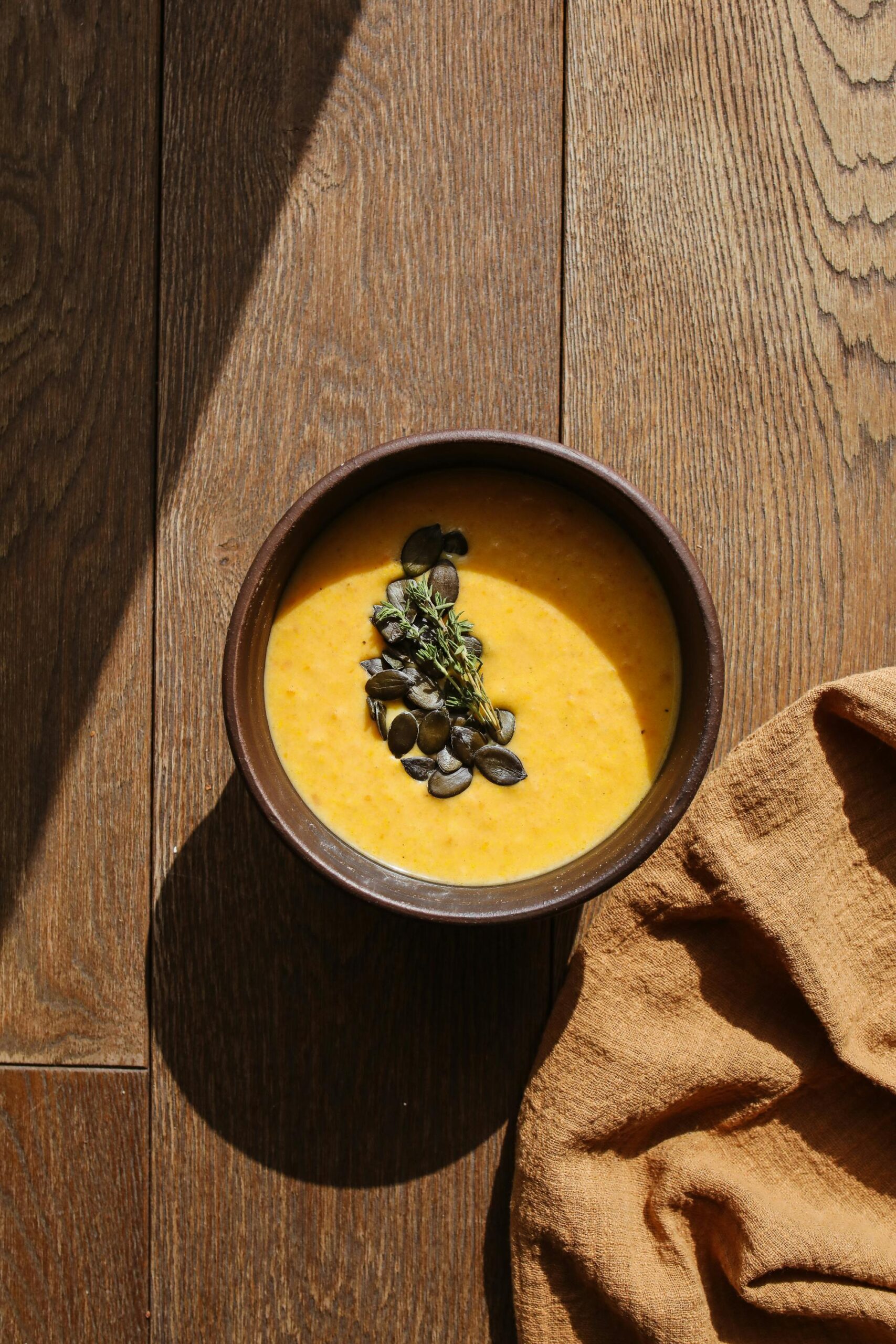 pexels-photo-5419035-5419035 A bowl of creamy pumpkin soup garnished with seeds on a wooden table.