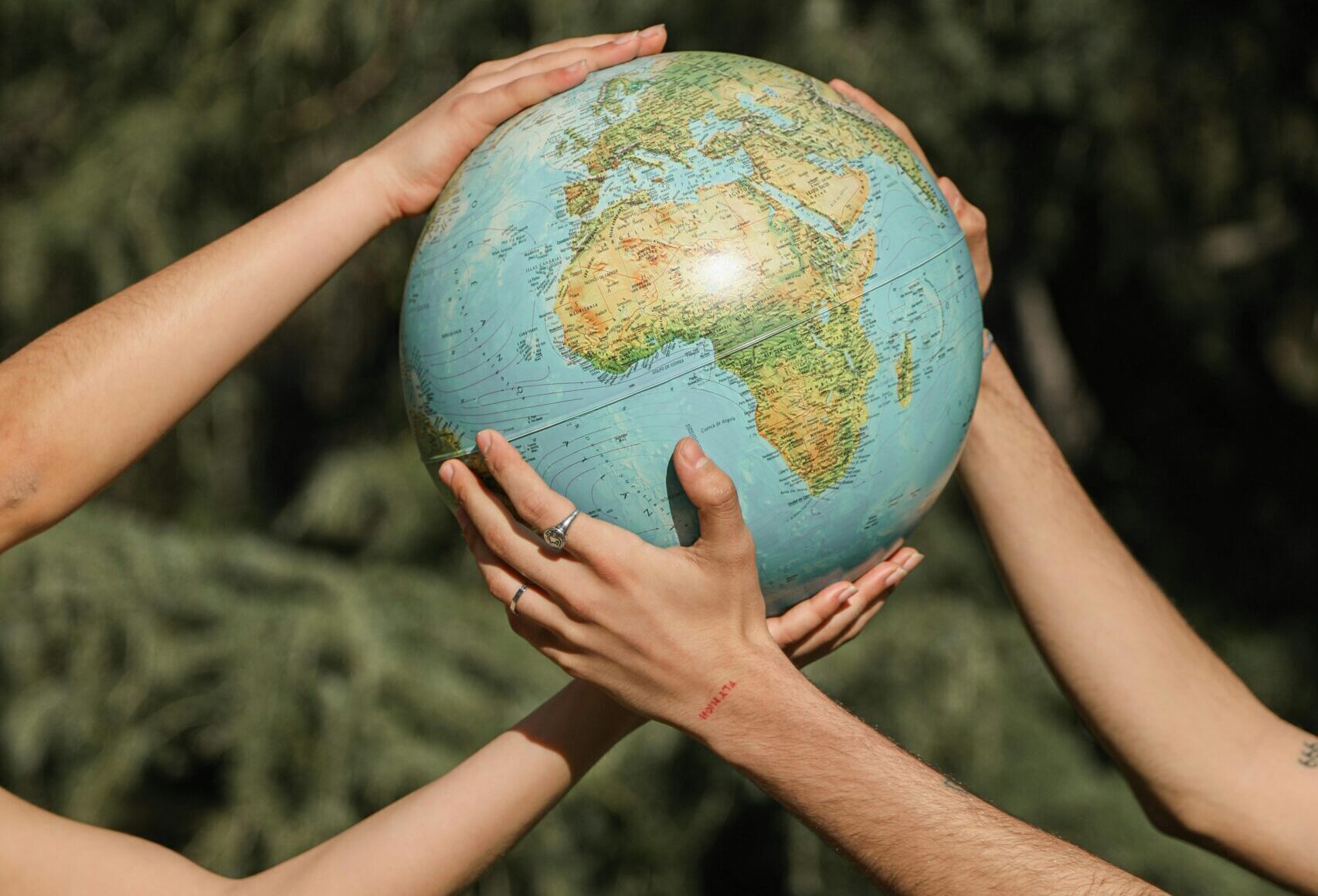 Four hands holding a globe outdoors, symbolizing unity and environmental conservation.