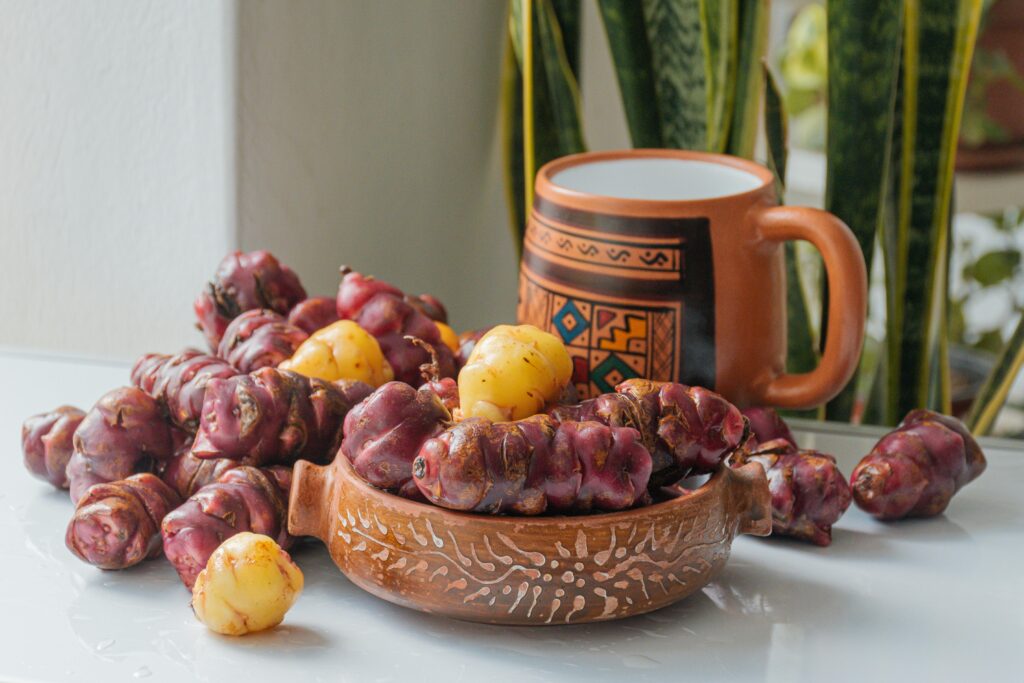 Olluco tubers with traditional Peruvian mug and ceramic bowl on a rustic table.