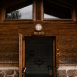 A rustic wooden exterior of a public restroom with an open door showing tiled interior.