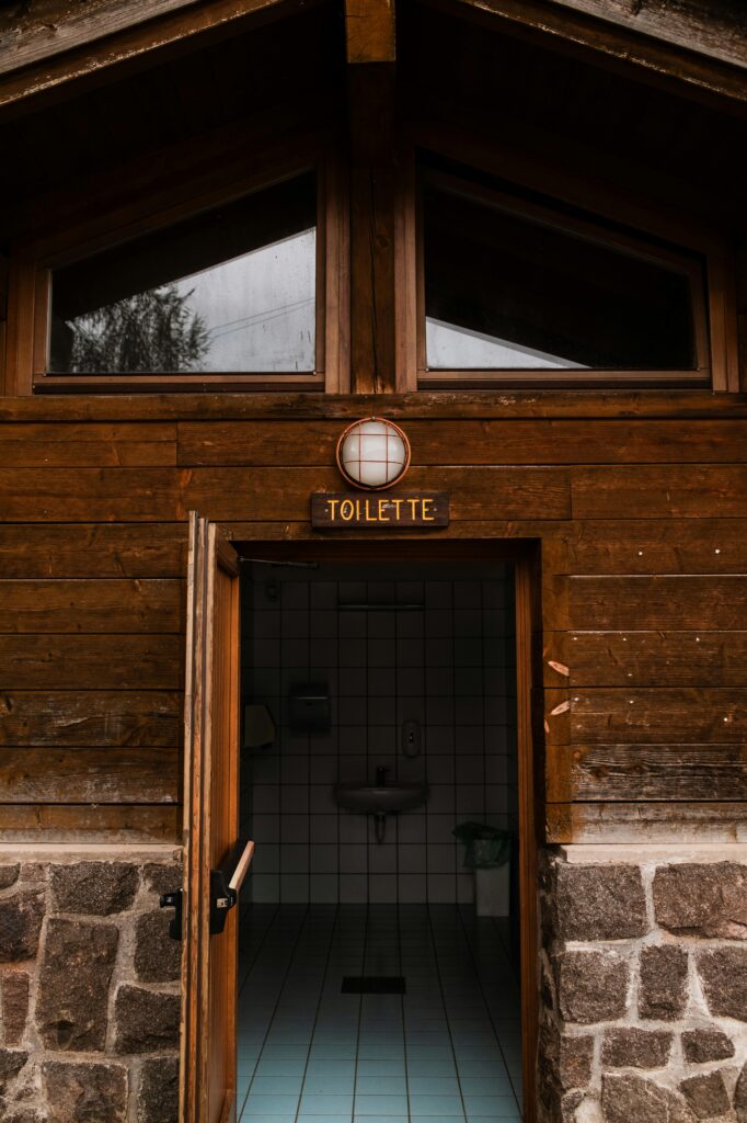 A rustic wooden exterior of a public restroom with an open door showing tiled interior.