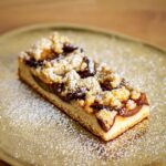 Mouthwatering apple crumble slice topped with powdered sugar on a golden platter.