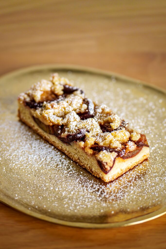 Mouthwatering apple crumble slice topped with powdered sugar on a golden platter.
