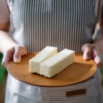 Close-up of a chef holding a wooden plate with two sticks of butter.