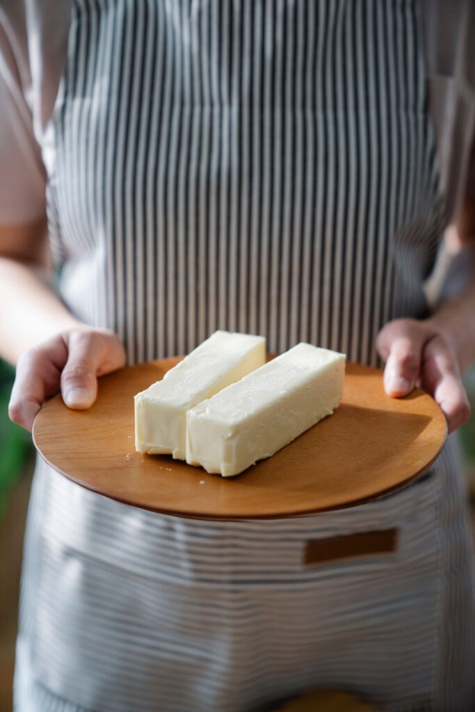 Close-up of a chef holding a wooden plate with two sticks of butter.